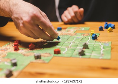 Smakhtino, Russia, December 2020: two men friends have fun playing the carcassonne board game late in the evening or at night. male hands and game cards and chips on table