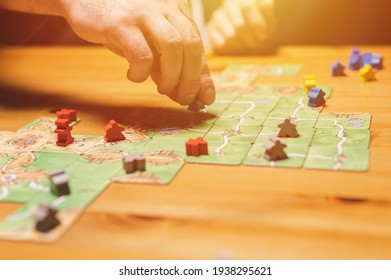Smakhtino, Russia, December 2020: two men friends have fun playing the carcassonne board game late in the evening or at night. male hands and game cards and chips on table. flare
