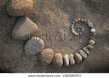Smal esoteric spiral made of colored pebbles on a grey rock background