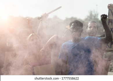 Small Activist Group Going Against Police Throwing Tear Gas. Multiethnic People Fighting For Human Rights. Black Lives Matter And No Racism Concept. Defocused Image For The Smoke.