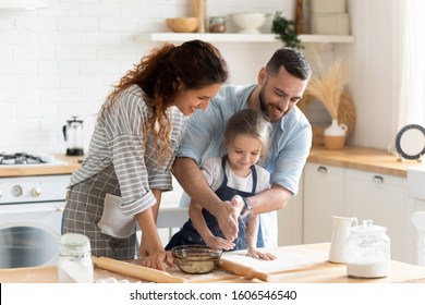 Small adorable kid girl preparing pie with loving caring parents on domestic kitchen, young family enjoy cooking process at home, teaching child, spend weekend together, help, happy parenthood concept - Powered by Shutterstock