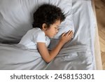 A small African American child dressed in pajamas is laying on a bed with a fluffy pillow beneath their head. The boy appears relaxed and comfortable in their surroundings.