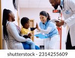 Small African American kid giving high five to pediatric nurse while being with his mother at doctor