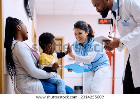 Small African American kid giving high five to pediatric nurse while being with his mother at doctor's office.