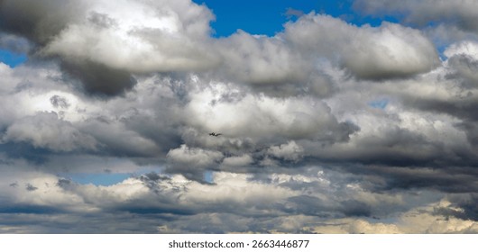  A small airplane flying through a dynamic sky filled with dramatic, large white and grey clouds against patches of blue.