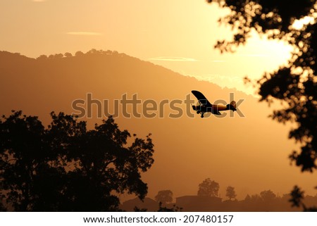 A small airplane flying through the golden yellow mountains preparing to land at sunset.