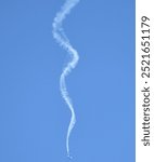 A small airplane performs a maneuver, leaving a long, swirling smoke trail in the clear blue sky.