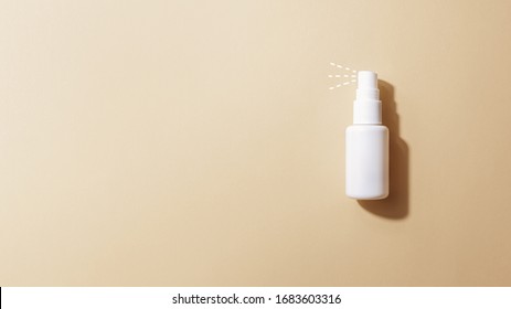 Small alcohol-based disinfecting antiseptic bottle spray spraying on beige background. Personal hygiene, disinfection, coronavirus protection concept mockup. Copy space, top view, flat lay