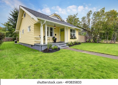 Small American Yellow House Exterior. Covered Porch With Stairs And Well Kept Lawn In The Front Yard. Northwest, USA