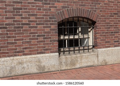 Small arched basement window facing sidewalk, wrought iron metal grate, horizontal aspect