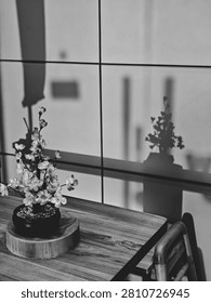 A small artificial sakura flower pot on a wooden desk creating a peaceful shadow on a grid pattern wall, Japanese style home decor.