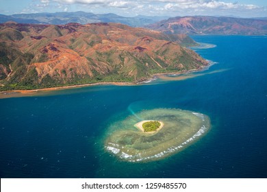 A small atoll islet with heart shaped coral reef off the east coast of Grande Terre island of New Caledonia, French overseas collectivity. Red green mountains hills full of nickel ore near Nakéty. - Powered by Shutterstock