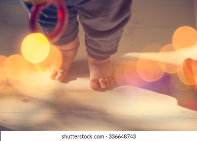 Small Baby Feet On Wooden Floor. First Steps Concept. Shallow Depth Of Field. Toned Photo With Bokeh And Copy Space.