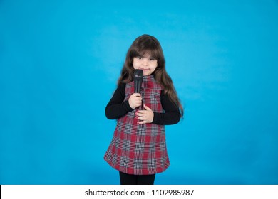 Small Baby Girl Holding Microphone And Smiling To Camera , In A Blue Background
