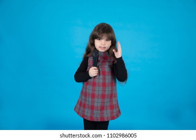 Small Baby Girl Holding Microphone And Talking While Rising Left Hand Up , In A Blue Background