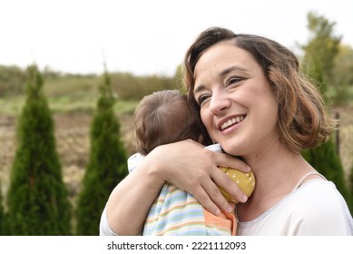 A Small Baby In His Mother's Arms With His Back Turned. A Small Child In His Mother's Arms. A Happy Young Woman With A Baby In Her Arms.