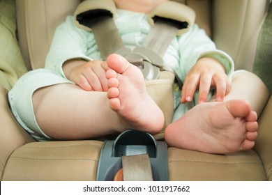 Small baby sitting in special car seat with safety seabelts, Safety in car concept, protection of child in travel, children feet in baby seat
