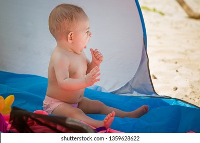 A Small Baby Is Sitting In A Tent Sheltered From The Sun On The Beach And Yawns.  Want To Sleep