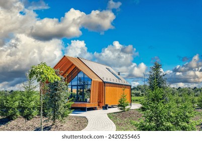 Small barnhouse on plot with green trees under cloudy sky. Modern small housing