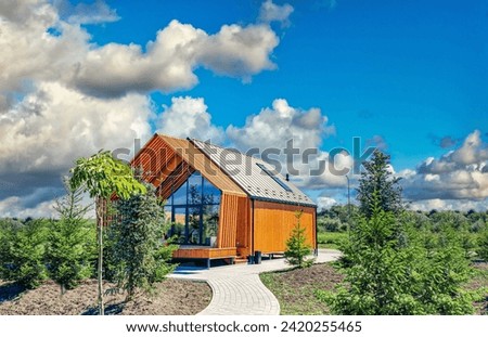 Small barnhouse on plot with green trees under cloudy sky. Modern small housing