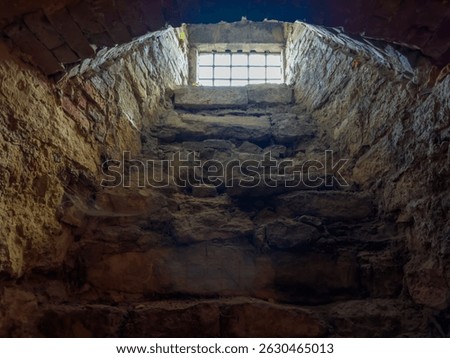 Small barred window to outside in arched opening of the dungeon of an old castle, view up from the inside