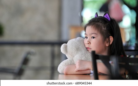 Small beautiful asian girl embraces an amusing bear cub sitting on the chair, a little girl try to be a model