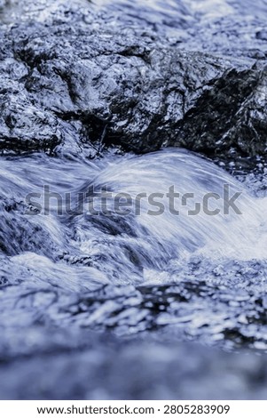 A small beautiful cascade of white bubbling water rushing down textured black volcanic river rocks.
