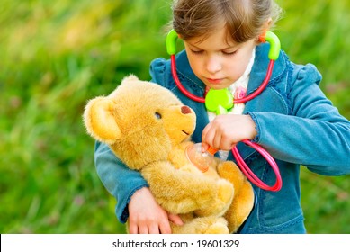 Small beautiful girl listens by means of stethoscope as heart of toy bear cub fights.