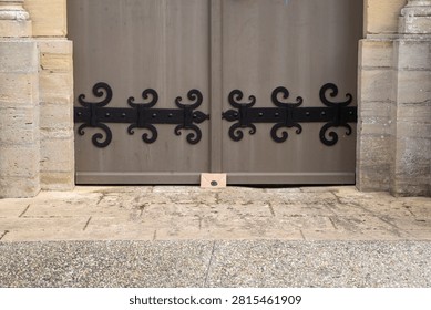 Small beige envelope closed with a dark wax seal and placed on the stone threshold of a large historic church door decorated with black wrought iron hinges.