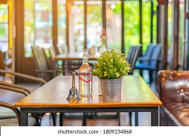A small bell for calling the waiter and artificial flowers in an aluminum pot and drinking water bottle placed on a table in a coffee shop.
