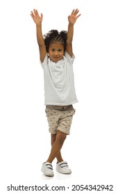 Small Black Boy In Sneakers, Shorts And Shirt Is Standing With Arms Raised And Looking At Camera. Front View. Full Length Studio Shot Isolated On White.