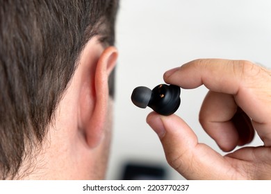 the small black earphones inserted into the ear of men close up. insert the earphone into the ear