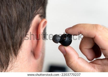 the small black earphones inserted into the ear of men close up. insert the earphone into the ear