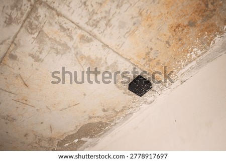 Small black electrical junction box mounted on a rough unpainted concrete ceiling at an unfinished construction site.