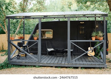 A small black trailer with a guitar on the porch, set against a serene backdrop, evokes a cozy musical moment - Powered by Shutterstock