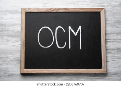 Small Blackboard With Abbreviation OCM (Organizational Change Management) On White Wooden Background, Top View