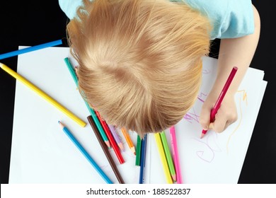 Small blond girl is drawing by pencils. Top view. 