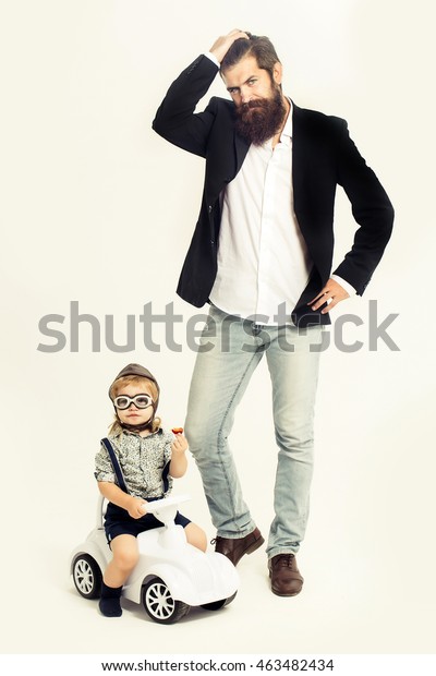 small blonde boy kid\
driver or pilot with long hair sitting on plastic toy cat in\
stylish shirt holding plum near bearded man father with beard\
isolated on white\
background