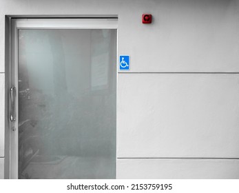 Small Blue Disable Handicap Toilet Sign On The Wall At Outdoor Restroom Door With Fire Alarm. Public Disabled Toilet With Frosted Glass Door.
