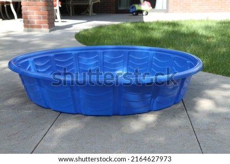 Small Blue Kids Pool on a Concrete Back Patio with Grass, Sunshine and a Brick Wall