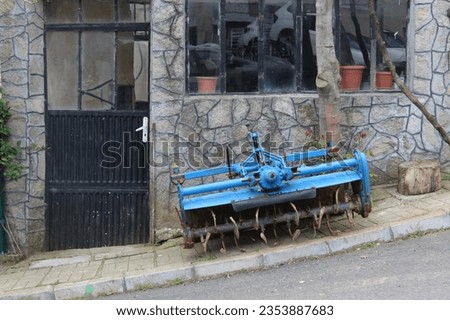 A small blue painted tractor placed in front of the village house. Photograph of industrial equipment vehicle used in the field.
