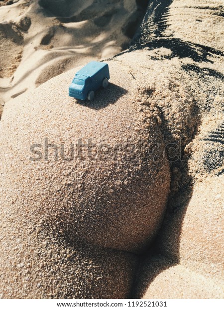 Small blue toy car on the sandy butt. Woman\
ass in the sand at sunny day in the\
beach