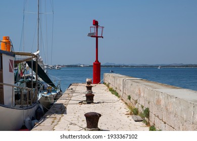 Small Boat Anchored Aside Picturesque Stone Peer With Red Steel Signal Post That Aids Safe Navigation Trough Shallow Waters And Easy Access To Krapanj Harbour On A Sunny Summer Day