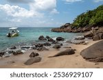 A small boat anchored near rocky shore with clear blue water and lush greenery on a sunny day in a tropical beach setting at Seychelles