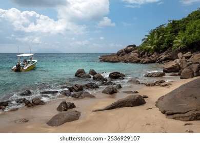 A small boat anchored near rocky shore with clear blue water and lush greenery on a sunny day in a tropical beach setting at Seychelles - Powered by Shutterstock