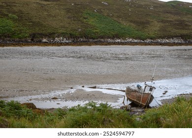 Small boat beached on the sea floor during low tide, Image shows a small wooden fishing boat resting on the sand  - Powered by Shutterstock