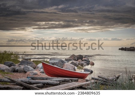 small boat on a beach, Image shows a small red dingy on a beach next to a wooden boat ramp with a number of smooth large rocks going out to a calm sea, during a summers sunset. August 2023