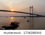 A small boat on the Houghly River as the sunsets behind the second Hoogly bridge. Kolkata, India