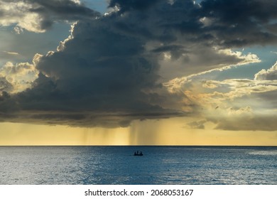 Small Boat Sailing In A Calm Sea And With The Storm And Clouds Approaching On The Horizon