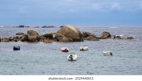 Small boats anchored near large rocks in Brittany in a calm sea under a cloudy sky. - Powered by Shutterstock